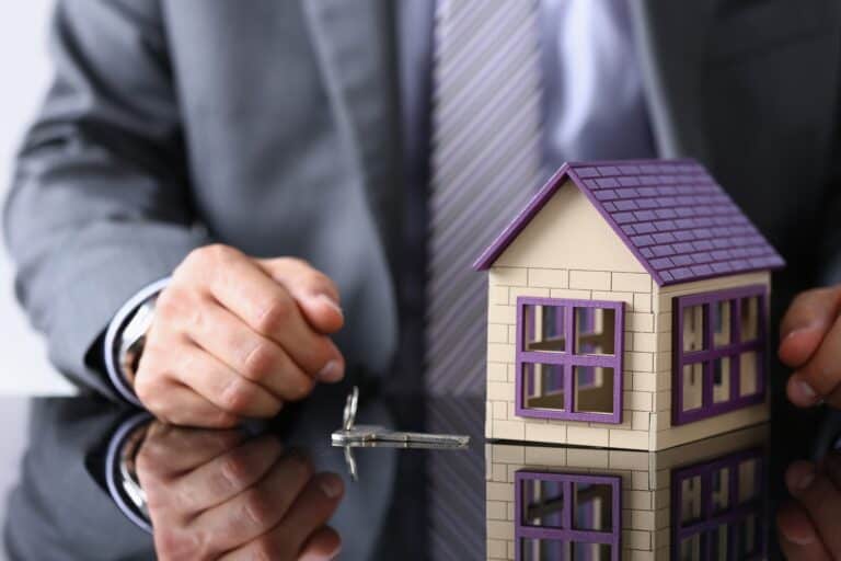 Cropped image of businessman with house figurine and key on the table in the concept of saving money when moving to Woolwich.